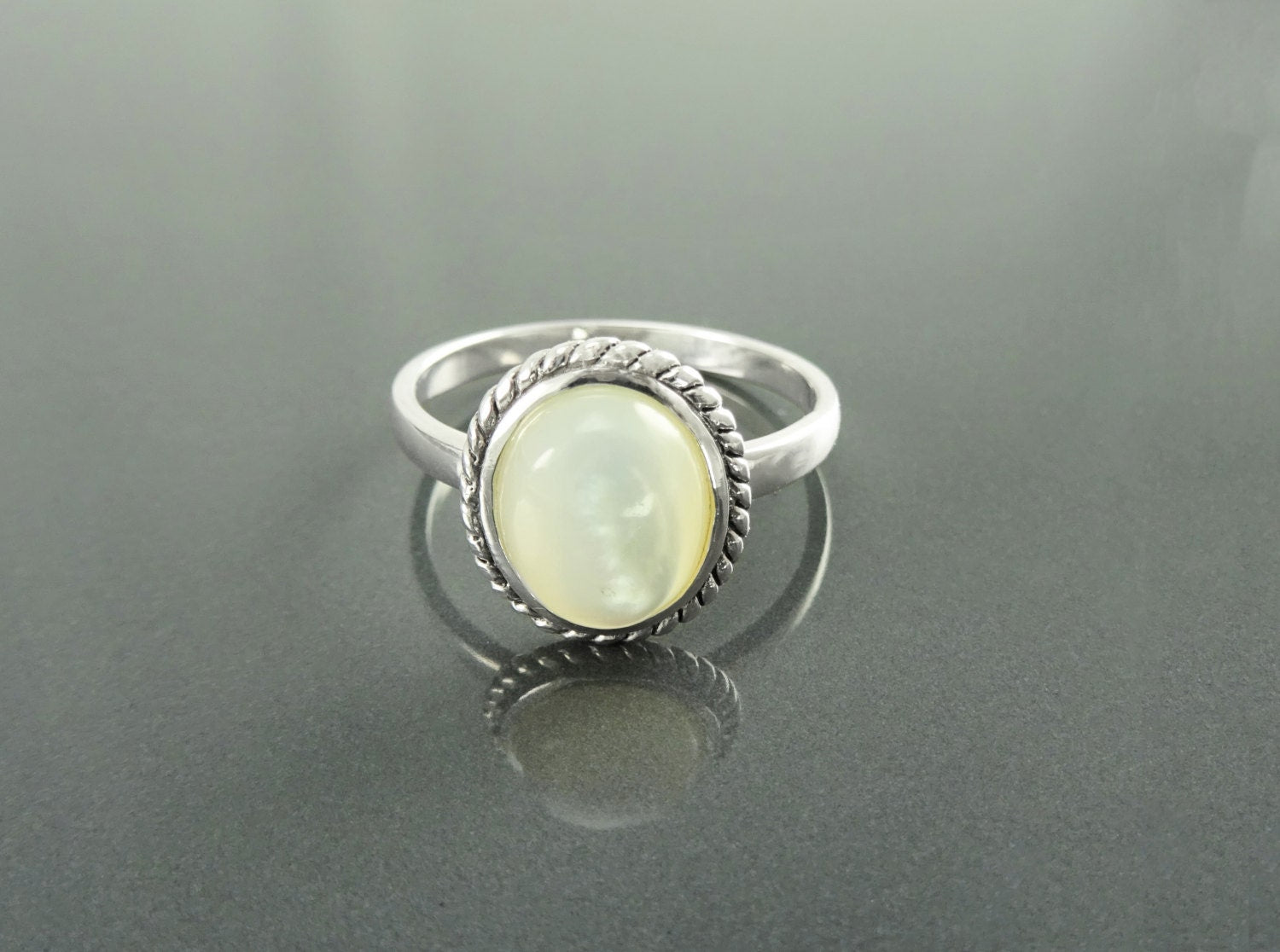 Une bague en argent avec une pierre en nacre blanche sertie dans un motif en forme de corde de style ancien. Un bijou artisanal fait main localement avec des matières naturelles. KRAMIKE est une boutique de qualité recommandée par ses milliers de clients.