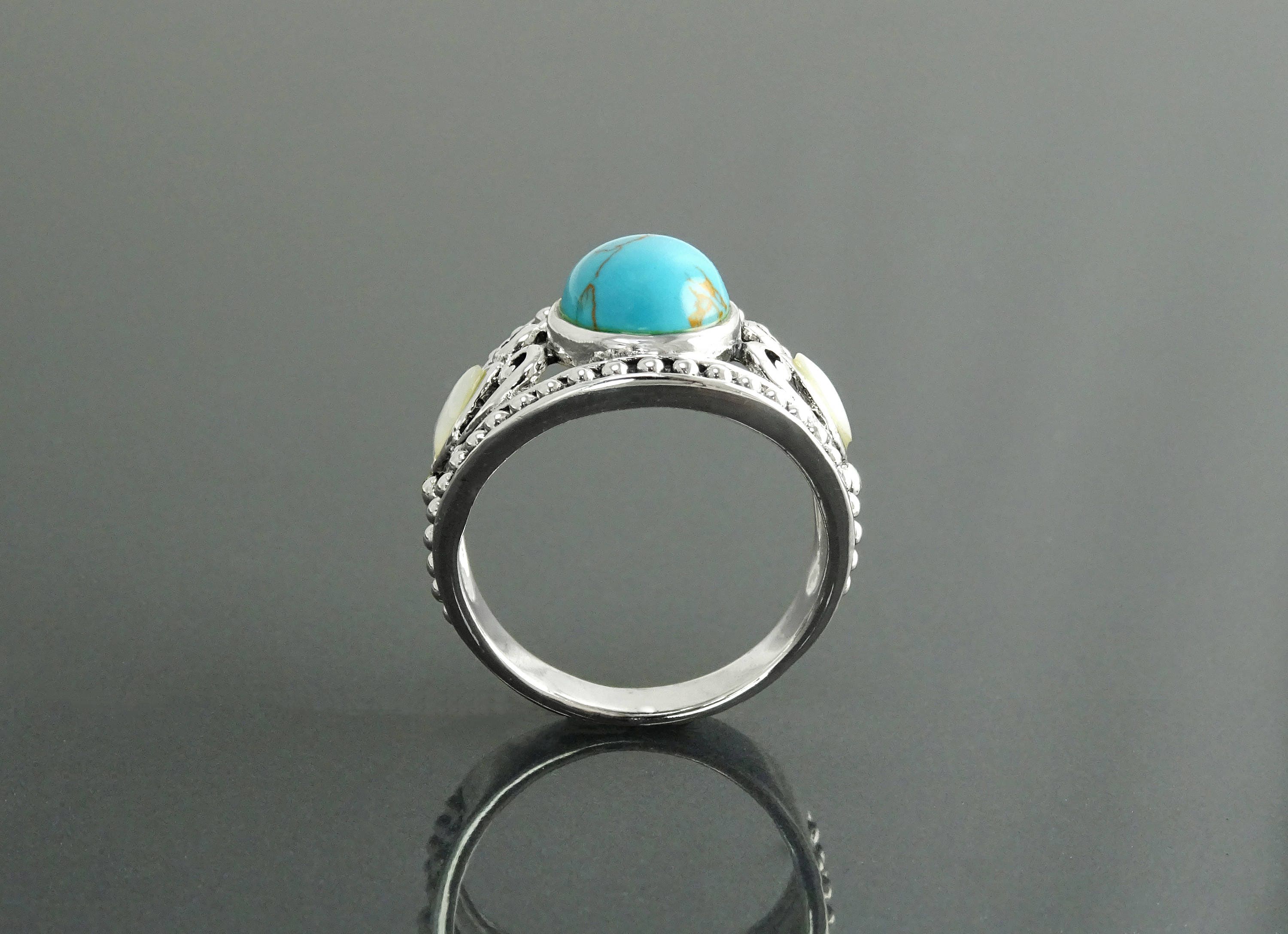 Une bague en argent 925 avec une pierre turquoise et deux petites nacres blanches. La bague a un filigrane détaillé vintage.