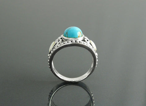 Une bague en argent 925 avec une pierre turquoise et deux petites nacres blanches. La bague a un filigrane détaillé vintage.