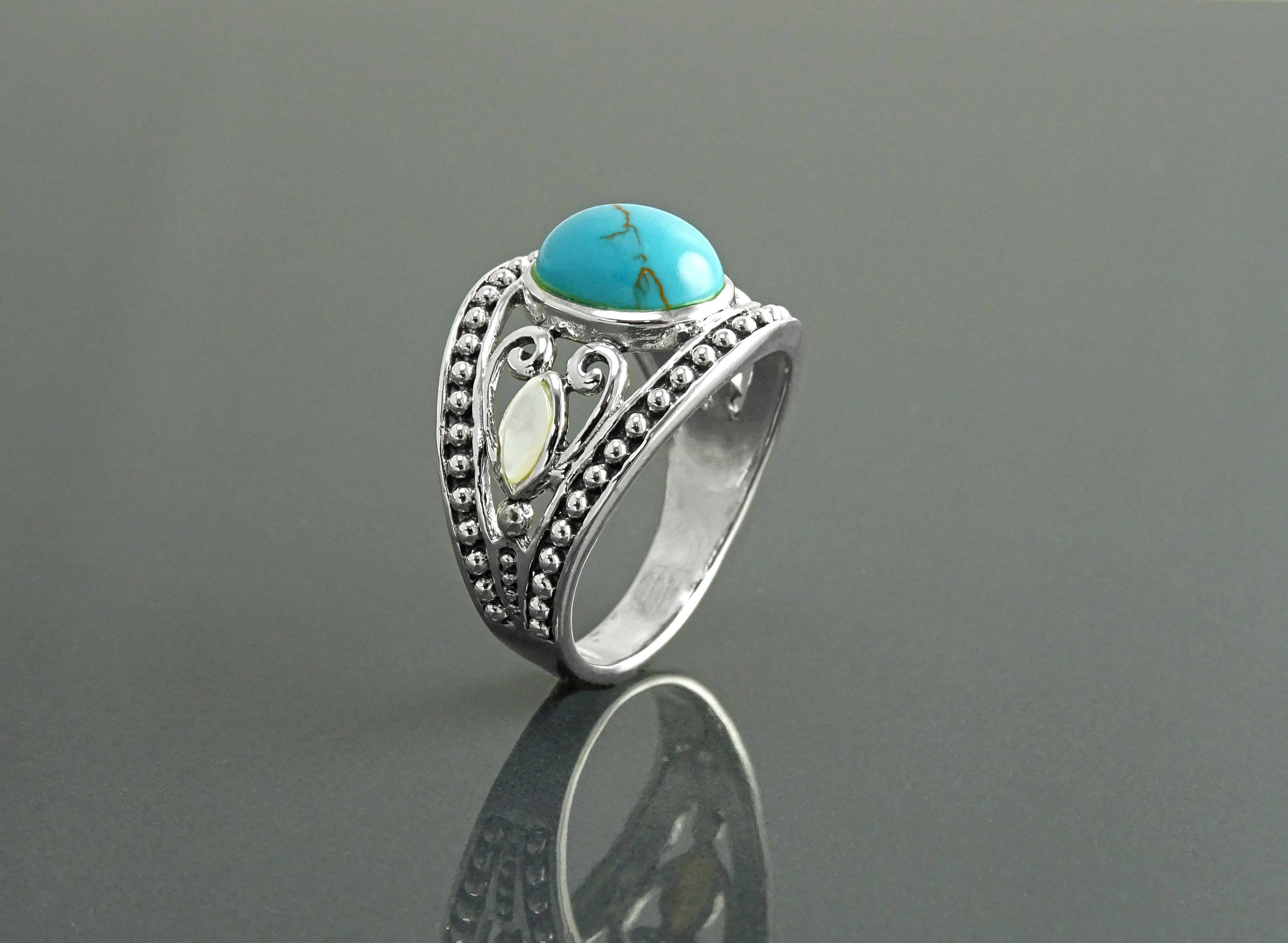 Une bague bohème en argent avec une pierre turquoise et une incrustation de nacre blanche. La bague est ornée d'un motif vintage perlé