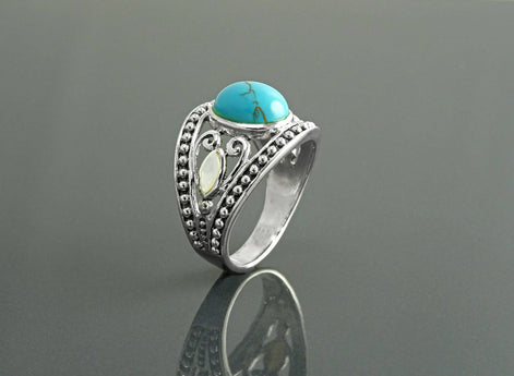 Une bague bohème en argent avec une pierre turquoise et une incrustation de nacre blanche. La bague est ornée d'un motif vintage perlé