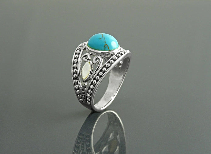 Une bague bohème en argent avec une pierre turquoise et une incrustation de nacre blanche. La bague est ornée d'un motif vintage perlé