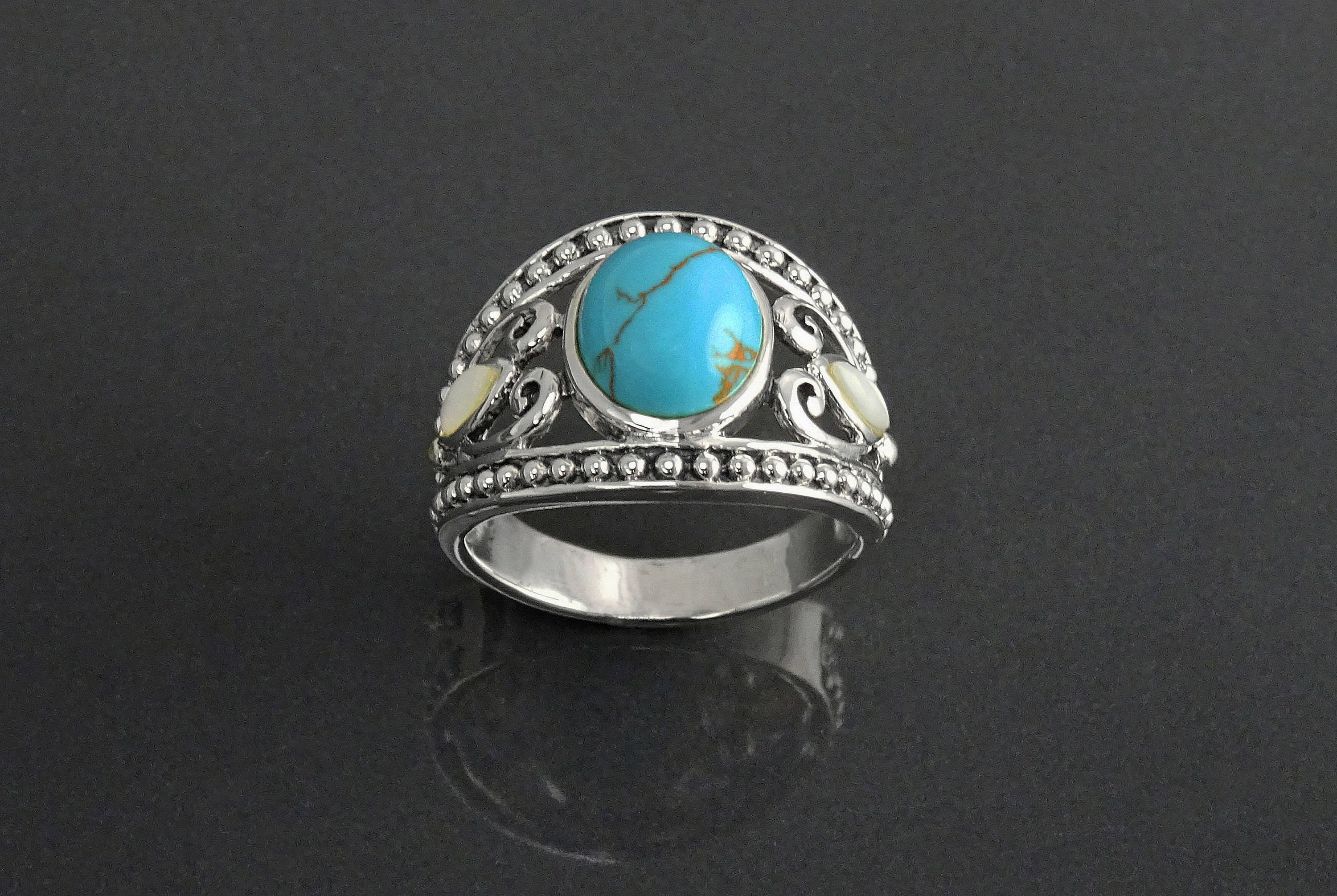 Une bague en argent avec une pierre turquoise et deux petites nacres blanches. La bague a un filigrane décoratif avec un bord perlé.