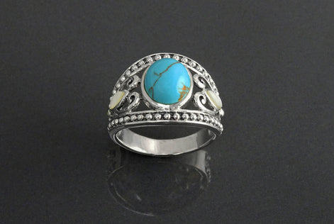 Une bague en argent avec une pierre turquoise et deux petites nacres blanches. La bague a un filigrane décoratif avec un bord perlé.