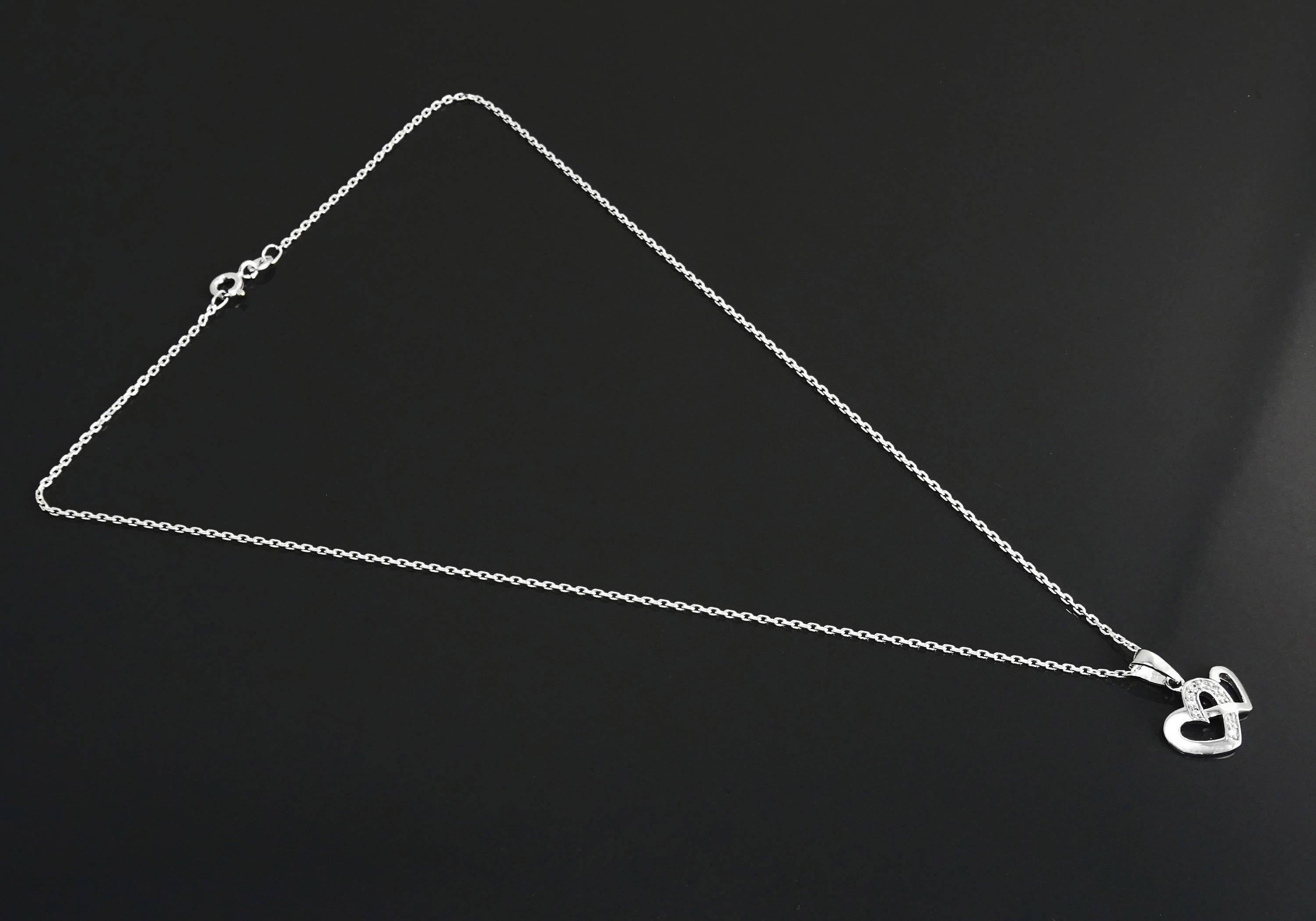 Un collier en chaîne argent avec un pendentif en forme de double cœur. Les cœurs sont entrelacés et ornés de petites pierres claires.