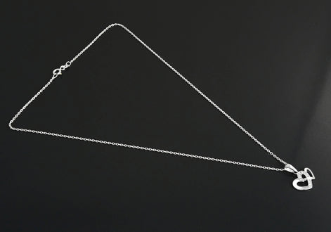 Un collier en chaîne argent avec un pendentif en forme de double cœur. Les cœurs sont entrelacés et ornés de petites pierres claires.