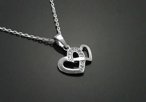 Un collier en argent avec un pendentif en forme de deux cœurs entrelacés. Les cœurs sont ornés de petites pierres scintillantes.
