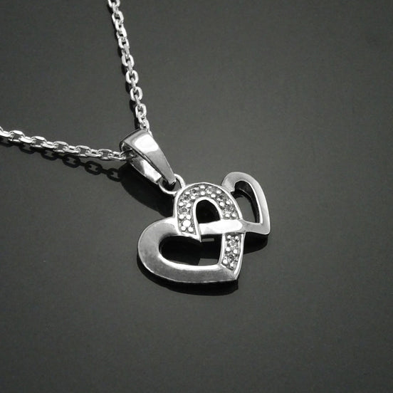 Un collier en argent avec un pendentif en forme de deux cœurs entrelacés. Les cœurs sont ornés de petites pierres scintillantes.