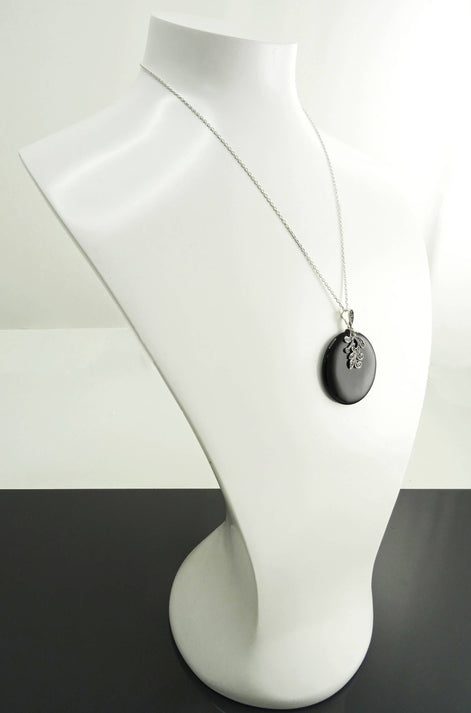 Un collier en chaîne argent 925 avec un pendentif rond en onyx noir et un motif floral argent massif de style vintage art nouveau. Le pendentif est présenté sur un buste de mannequin blanc.