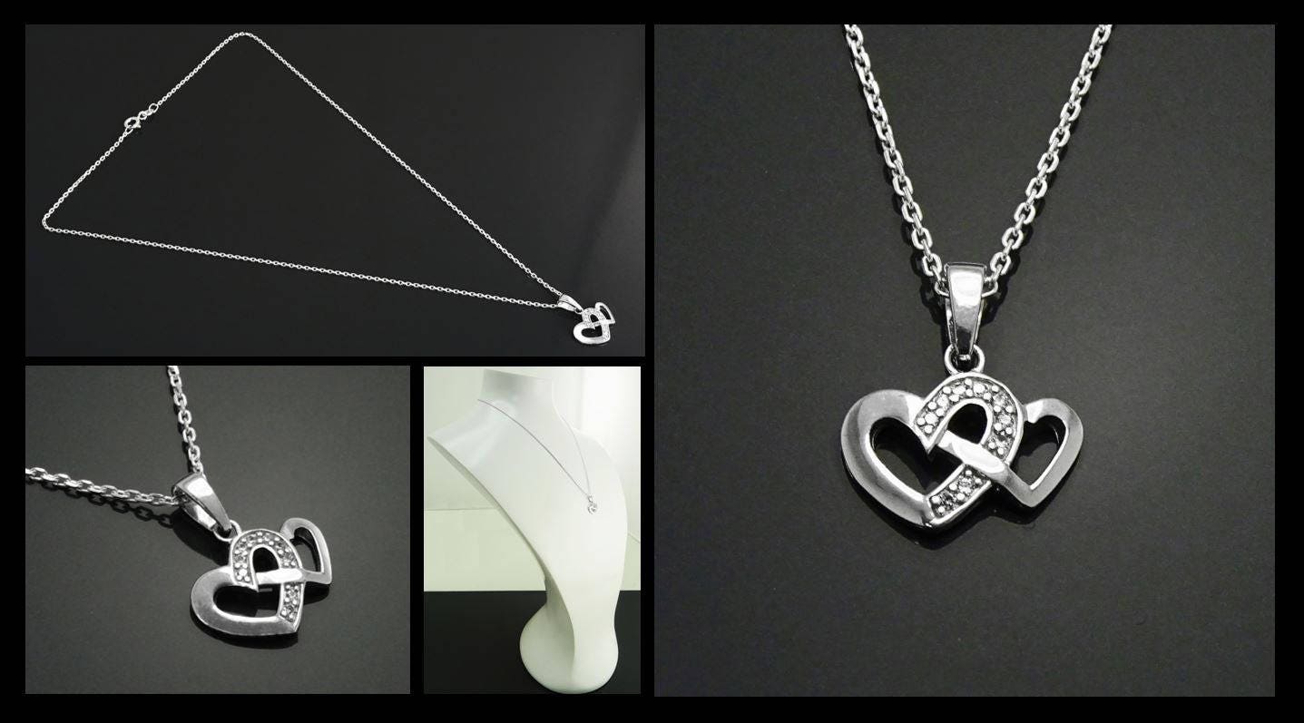 Un collier en argent avec un pendentif en forme de deux cœurs entrelacés sertis de petites pierres claires.