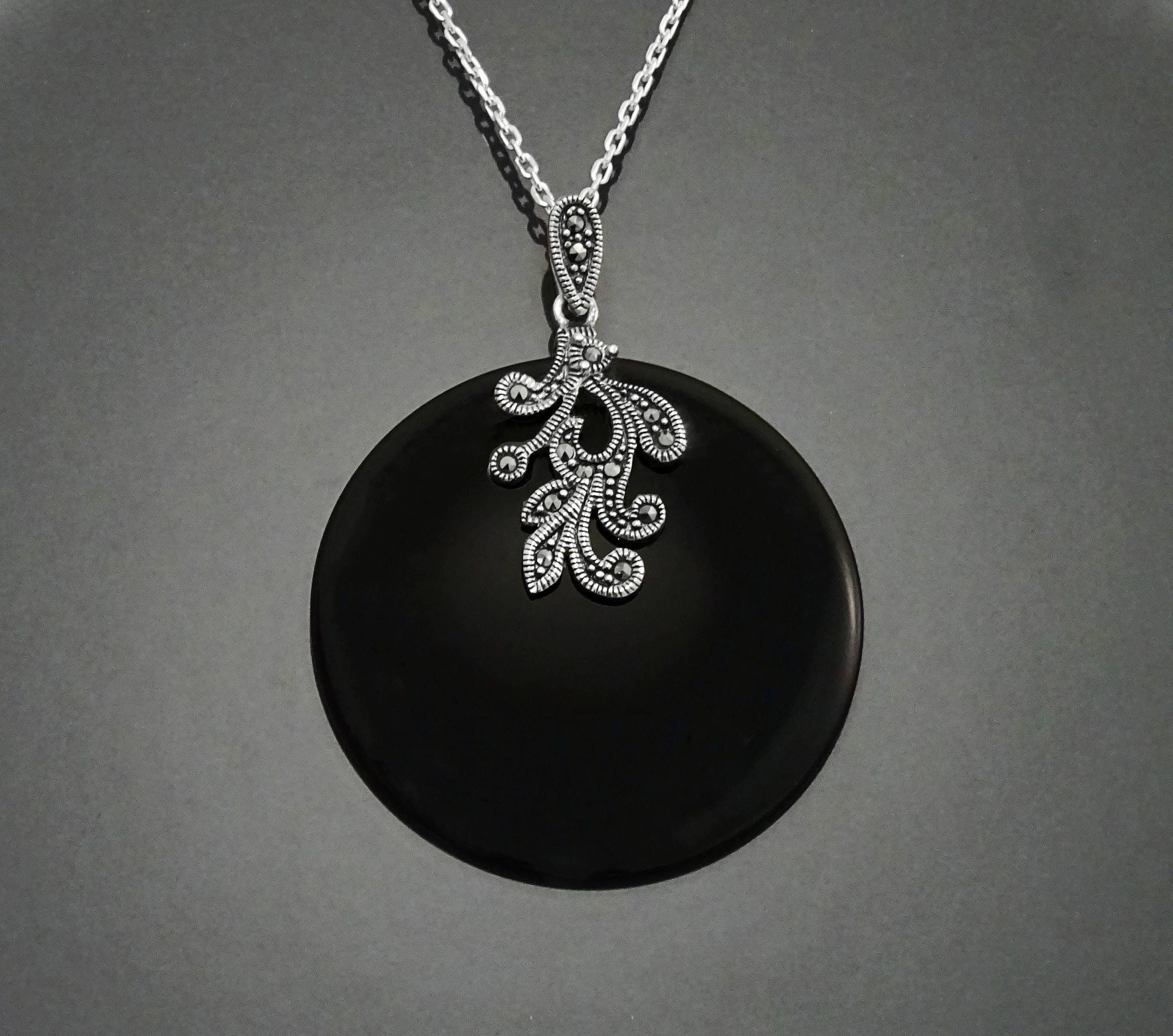 Un collier en argent avec un pendentif en onyx noir orné d'un motif vintage Art Deco détaillé en marcassite.