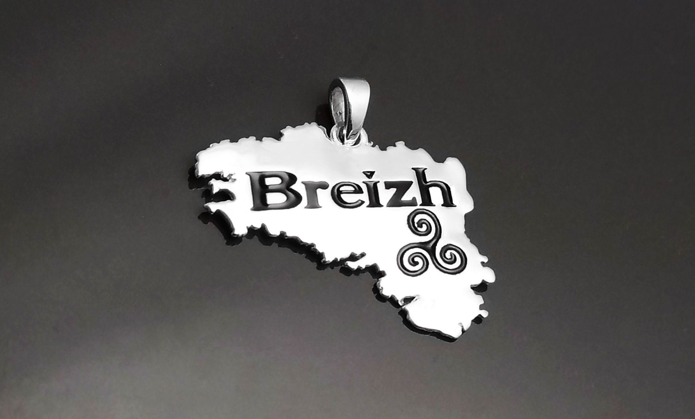 A silver pendant shaped like the region of Brittany, France, with the word "Breizh" and a Celtic triskelion symbol engraved in black.
Brand: KRAMIKE
Type of jewelry: Pendant
Metal: 925 sterling silver
Size: 20×30 mm
Handmade: yes
Ships from: France
Necklace: chain on request

Brittany pendant, French regional gift, French Souvenir, Brittany gift, Breizh Necklace, Breizh pendant, Brittany jewelry, French Brittany gift, Brittany necklace, Brittany map, Brittany symbol