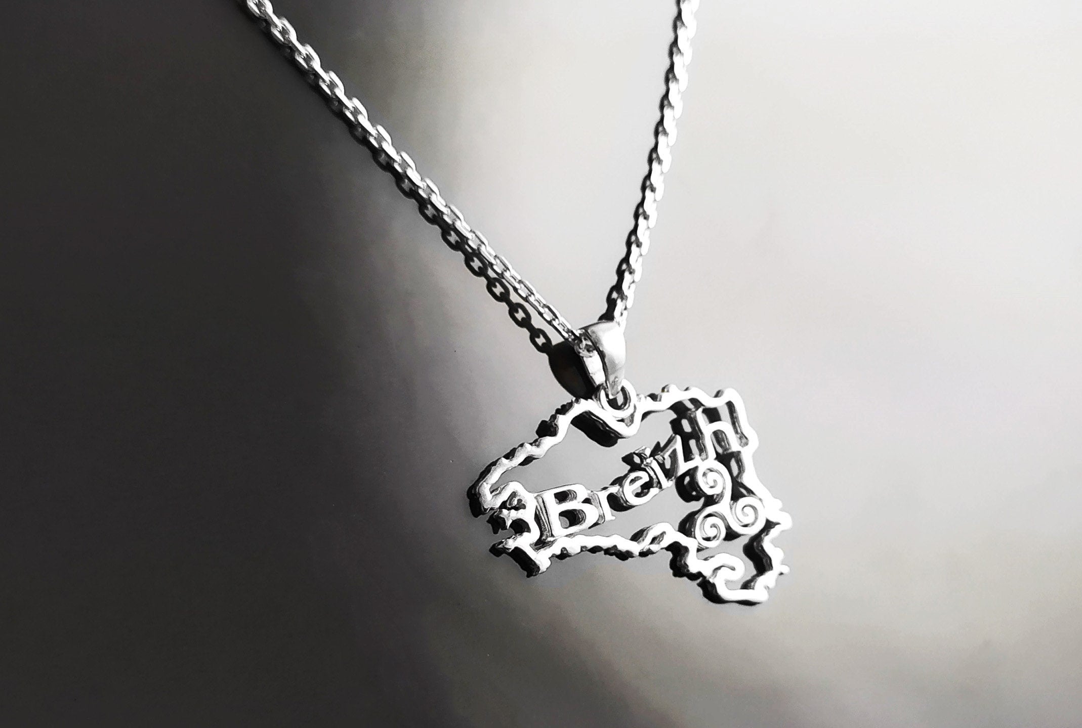 A silver necklace with a pendant shaped like the outline of the state of  'Breizh' (Brittany) in France. The pendant has the word 'Breizh' written inside the outline.
Brand: KRAMIKE
Product: Brittany map necklace / Breizh pendant
Metal: 925 sterling silver
Pendant size: 3.0 × 2.0 cm
Weight: 3.6 g
Symbol: Triskel (center detail)
Chain options: 45 cm / 50 cm / 55 cm
Ships from: France
Tracking: included