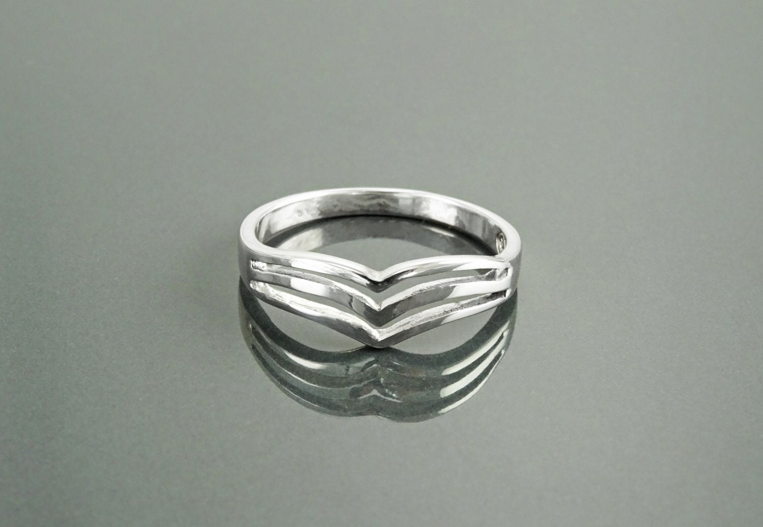 Une bague en argent 925 avec un motif triple chevron. La bague est en métal lisse et poli et a un style simple et moderne.