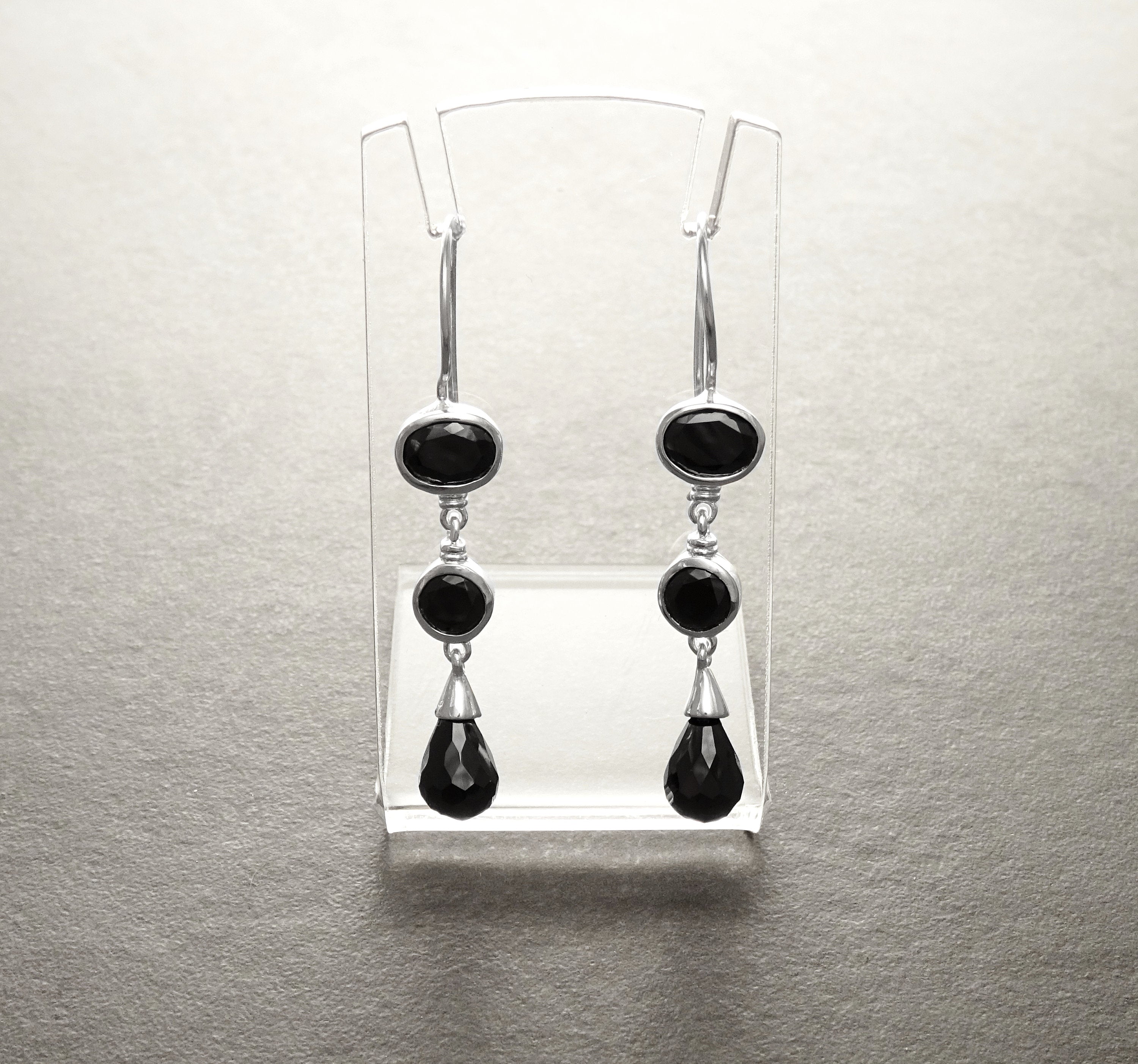 Une paire de boucles d'oreilles pendantes crochets français en argent 925 avec trois pierres précieuses ovales noires sur chaque boucle d'oreille. La pierre précieuse du bas est en forme de larme.
