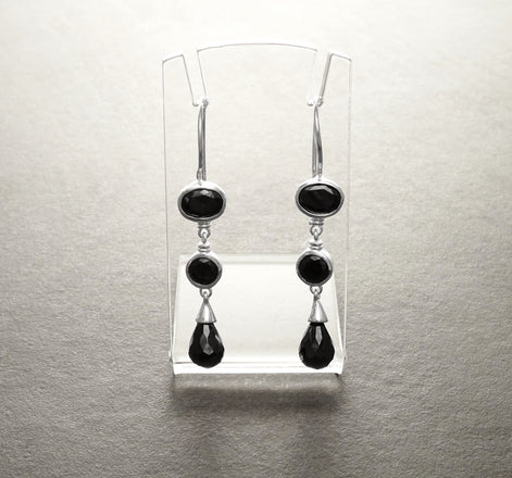 Une paire de boucles d'oreilles pendantes crochets français en argent 925 avec trois pierres précieuses ovales noires sur chaque boucle d'oreille. La pierre précieuse du bas est en forme de larme.
