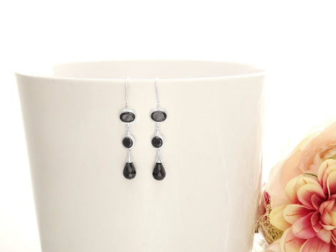 Boucles d'oreilles pendantes en argent 925 avec trois pierres Cz zirconium noires. La pierre du haut est ronde, la pierre du milieu est ovale et la pierre du bas a la forme d'une larme. Longues boucles d'oreilles modernes à crochets vendues par KRAMIKE Paris