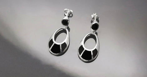 Une paire de boucles d'oreilles pendantes en argent 925 avec des onyx noirs. Les boucles d'oreilles ont un design simple, avec une petite pierre noire en haut et des plus grandes pierres noires sur la forme ovale du bas.
