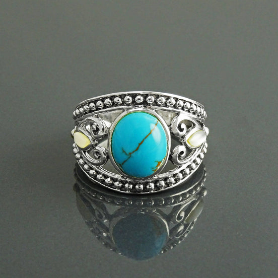 Une bague en argent 925 avec une pierre turquoise sertie dans un motif de filigrane décoratif. La bague a une bande perlée et deux petites nacres blanches de chaque côté de la pierre turquoise.