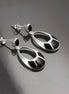 Une paire de boucles d'oreilles pendantes ovales en argent 925 avec des pierres onyx noires. Les pierres ont un motif géométrique.