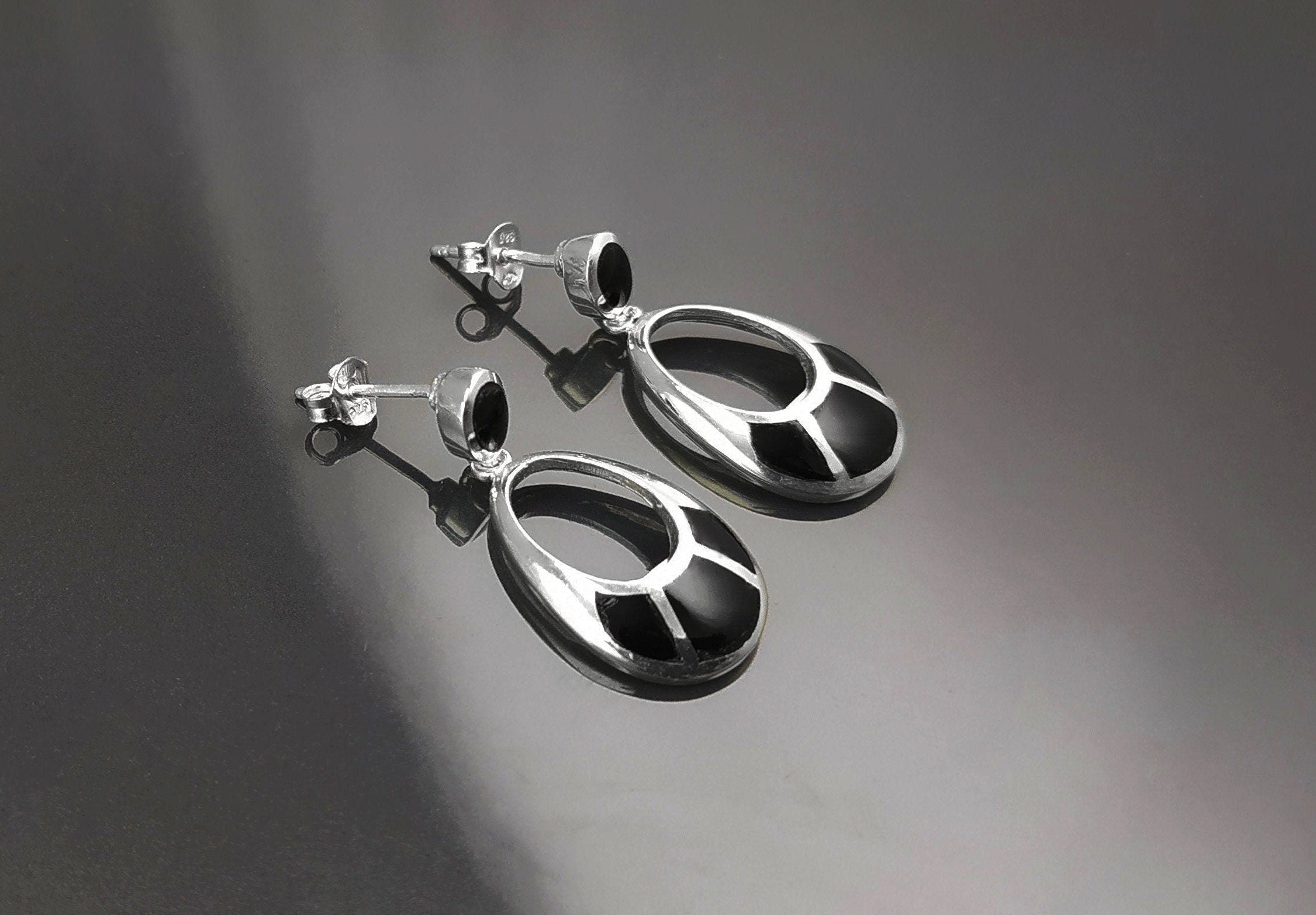 Une paire de boucles d'oreilles pendantes ovales en argent 925 avec des pierres onyx noires. Les pierres ont un motif géométrique.