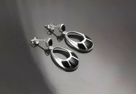 Une paire de boucles d'oreilles pendantes ovales en argent 925 avec des pierres onyx noires. Les pierres ont un motif géométrique.