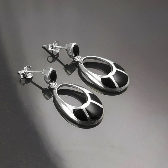 Une paire de boucles d'oreilles pendantes ovales en argent 925 avec des pierres onyx noires. Les pierres ont un motif géométrique.