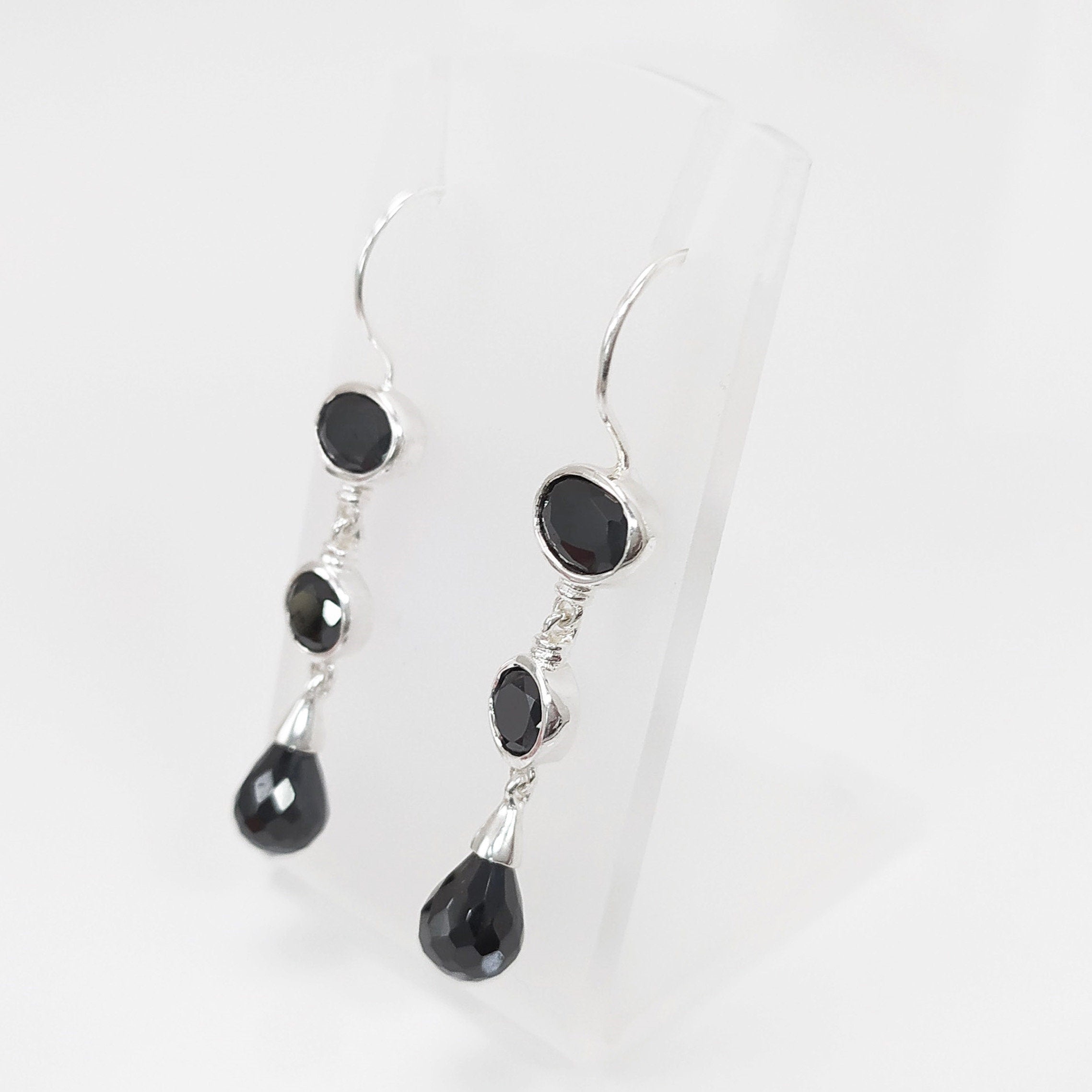 Boucles d'oreilles pendantes en argent massif avec trois pierres Cz zirconium noires. La pierre du haut est ronde, la pierre du milieu est ovale et la pierre du bas a la forme d'une larme. Longues boucles d'oreilles modernes à crochets vendues par KRAMIKE Paris