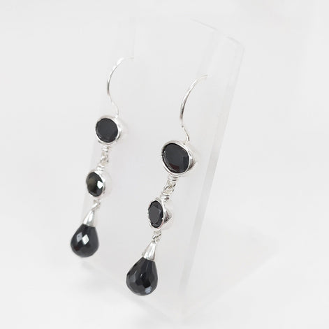 Boucles d'oreilles pendantes en argent massif avec trois pierres Cz zirconium noires. La pierre du haut est ronde, la pierre du milieu est ovale et la pierre du bas a la forme d'une larme. Longues boucles d'oreilles modernes à crochets vendues par KRAMIKE Paris