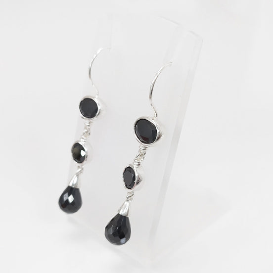 Boucles d'oreilles pendantes en argent massif avec trois pierres Cz zirconium noires. La pierre du haut est ronde, la pierre du milieu est ovale et la pierre du bas a la forme d'une larme. Longues boucles d'oreilles modernes à crochets vendues par KRAMIKE Paris