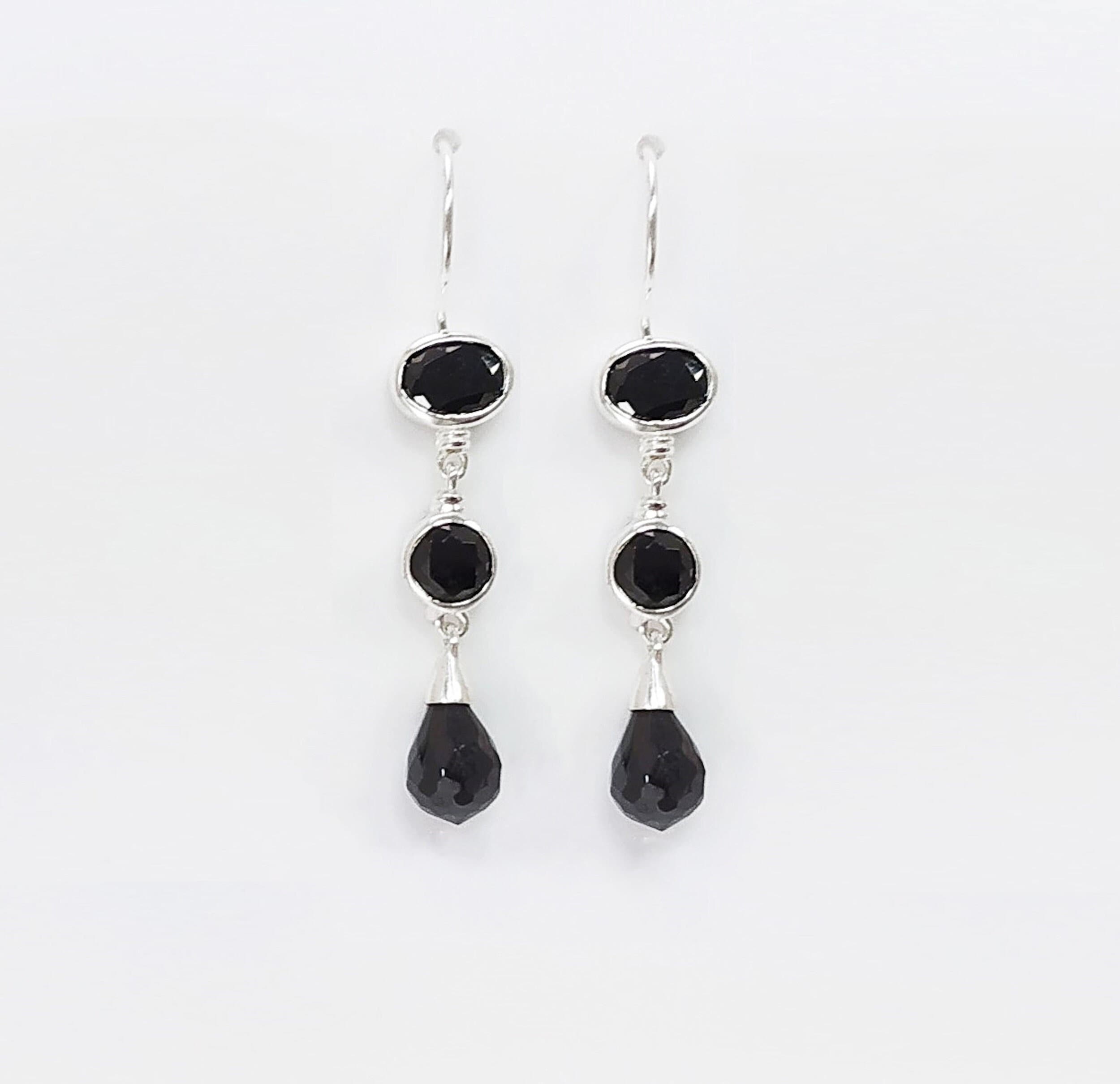 Une paire de boucles d'oreilles pendantes en argent 925 avec trois pierres Cz zirconium noires. La pierre du haut est ronde, la pierre du milieu est ovale et la pierre du bas a la forme d'une larme. Longues boucles d'oreilles à crochets en  modernes vendues par KRAMIKE Paris