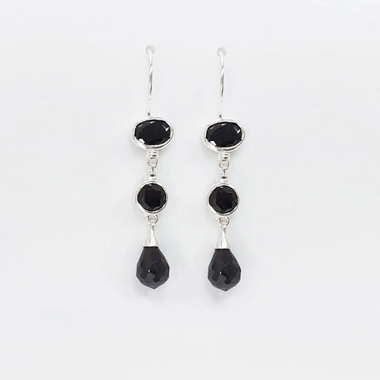 Une paire de boucles d'oreilles pendantes en argent 925 avec trois pierres Cz zirconium noires. La pierre du haut est ronde, la pierre du milieu est ovale et la pierre du bas a la forme d'une larme. Longues boucles d'oreilles à crochets en  modernes vendues par KRAMIKE Paris