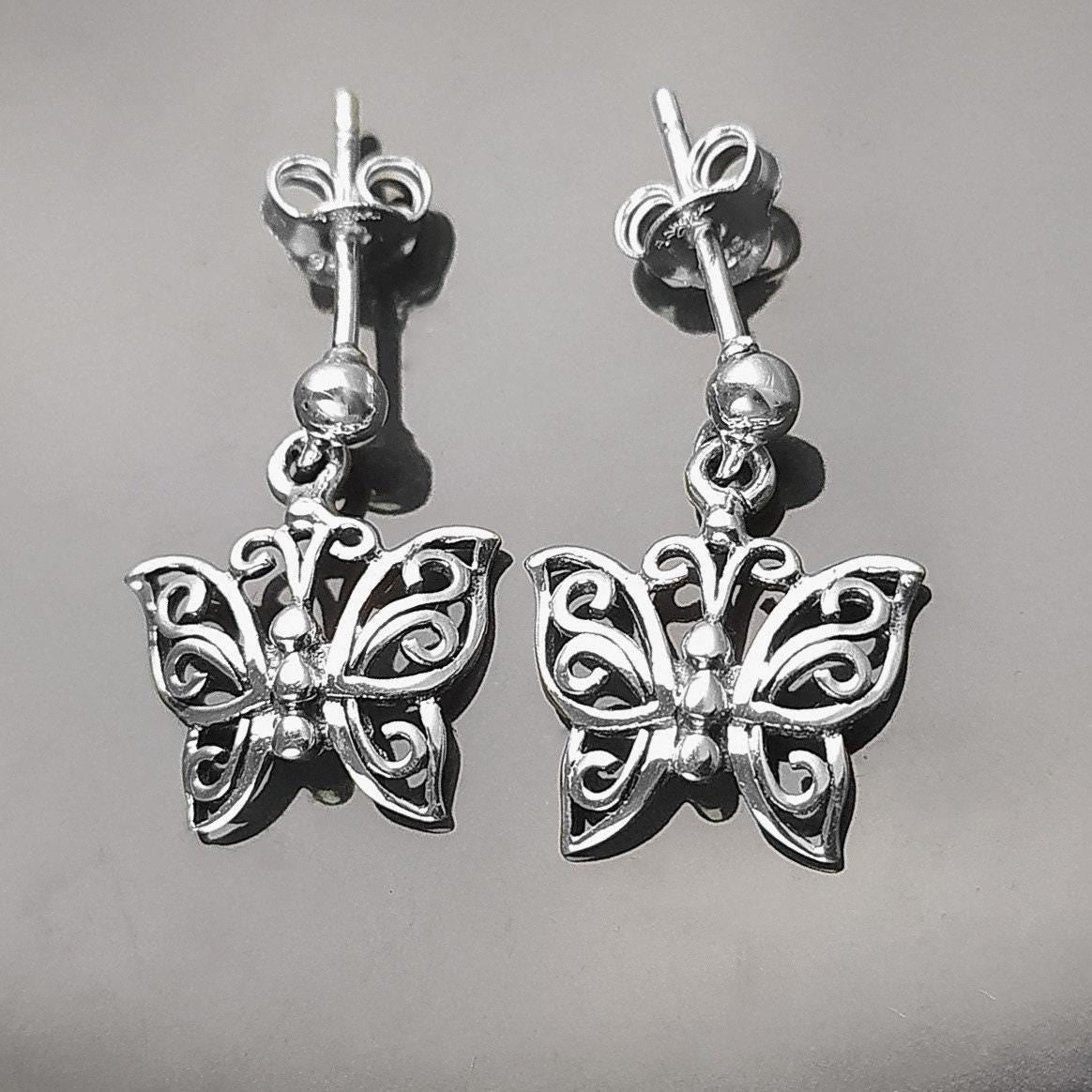 Une paire de boucles d'oreilles pendantes en argent en forme de papillon. Les boucles d'oreilles présentent un design délicat et complexe avec un motif de filigrane. 
Boucles d'oreilles papillon en Argent 925, Symbole de la Métamorphose, du renouvellement et du commencement d'un nouveau chapitre de vie.
Boucles vu de face. Des Papillons en filigrane sur tige.
Durable, fait main, local. Créateurs sûrs. Boutique aux milliers d'avis.