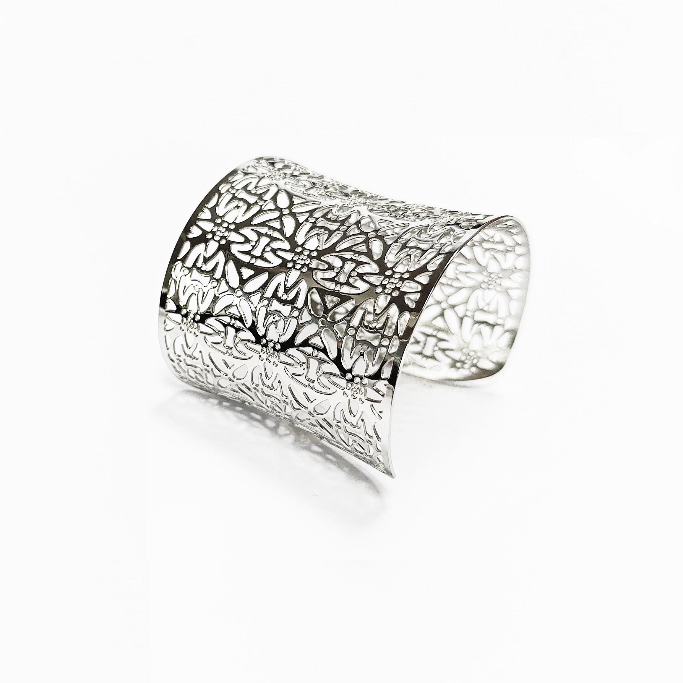 Angle view — A silver cuff bracelet with a floral cutout design. The wide bracelet curves slightly and features an intricate pattern of stylized flowers and leaves. The metal has a polished, reflective surface.

Brand: KRAMIKE
Type of jewelry: cuff / statement armor cuff
Metal: stainless steel
Color: silver-tone
Style: Filigree floral lace / modern boho
Diameter: 66 mm
Width: 60 mm
Ships from: France