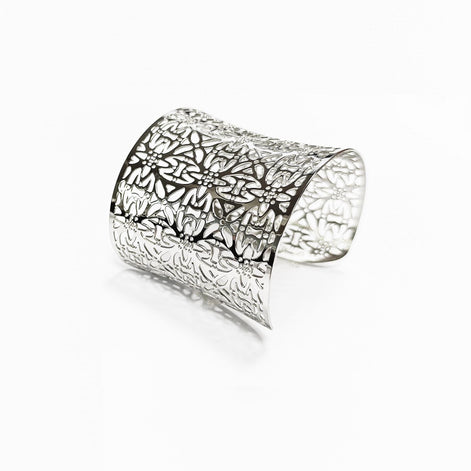 Angle view — A silver cuff bracelet with a floral cutout design. The wide bracelet curves slightly and features an intricate pattern of stylized flowers and leaves. The metal has a polished, reflective surface.

Brand: KRAMIKE
Type of jewelry: cuff / statement armor cuff
Metal: stainless steel
Color: silver-tone
Style: Filigree floral lace / modern boho
Diameter: 66 mm
Width: 60 mm
Ships from: France