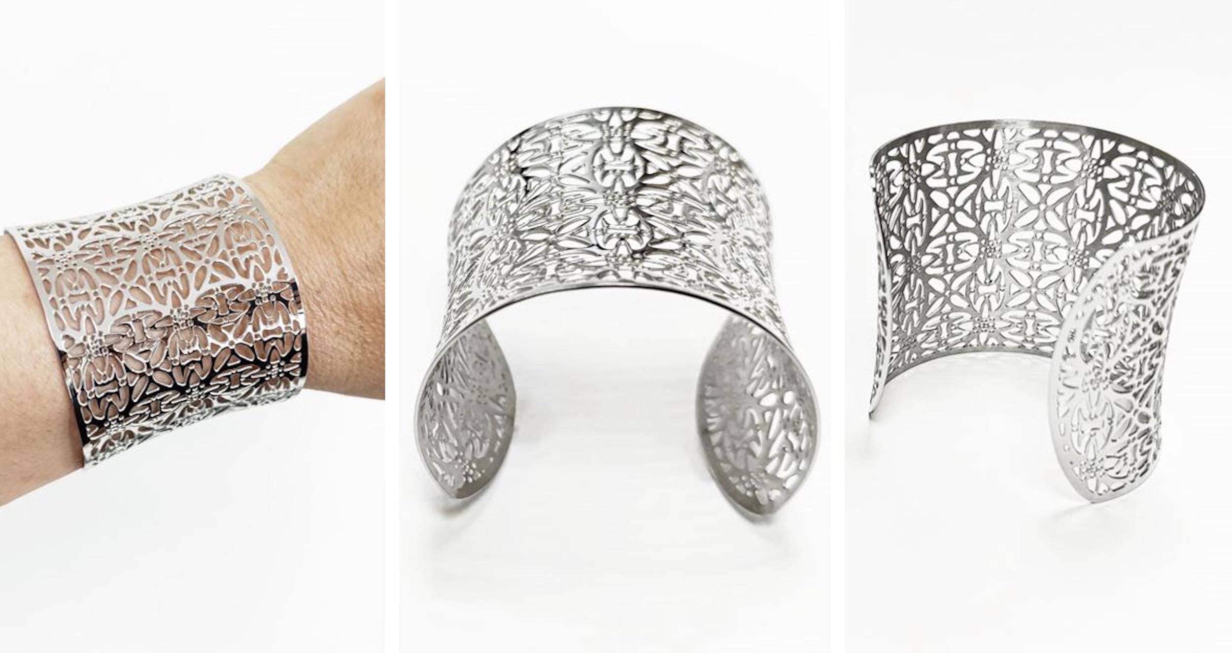 A silver-colored cuff bracelet with an openwork floral design. The wide bracelet is shown on a wrist and in two other views. The metal jewelry has a curved shape and intricate cut-out patterns.
Brand: KRAMIKE
Type of jewelry: cuff / statement armor cuff
Metal: stainless steel
Color: silver-tone
Style: Filigree floral lace / modern boho
Diameter: 66 mm
Width: 60 mm
Ships from: France