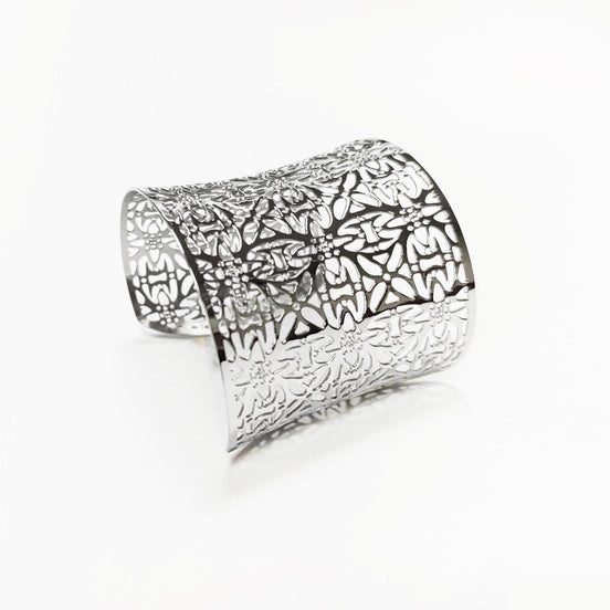 Angle view — Silver cuff bracelet with a floral pattern. The wide bracelet has a curved shape and is made of a shiny, reflective metal. The openwork design allows light to pass through, creating a delicate and intricate look.

Brand: KRAMIKE
Type of jewelry: cuff / statement armor cuff
Metal: stainless steel
Color: silver-tone
Style: Filigree floral lace / modern boho
Diameter: 66 mm
Width: 60 mm
Ships from: France