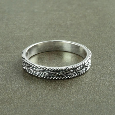 Une bague en argent massif 925 avec un motif tressé. 
La bague présente un motif détaillé de brins entrelacés, créant une surface texturée. Plusieurs vues mettent en valeur le savoir-faire et le design complexe de la bague.
Vu bague posée. fond gris.
Bijou artisanal durable. Fait main local. Boutique de confiance recommandée.