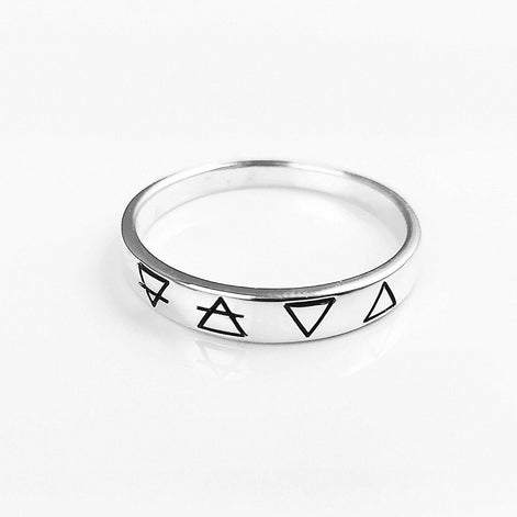 Une bague en argent avec quatre symboles gravés : un cercle avec une ligne qui le traverse, un triangle, un triangle inversé et un triangle avec une ligne qui le traverse.
VU D'en haut.
Bijou artisanal durable. Fait main local. Boutique de confiance recommandée.