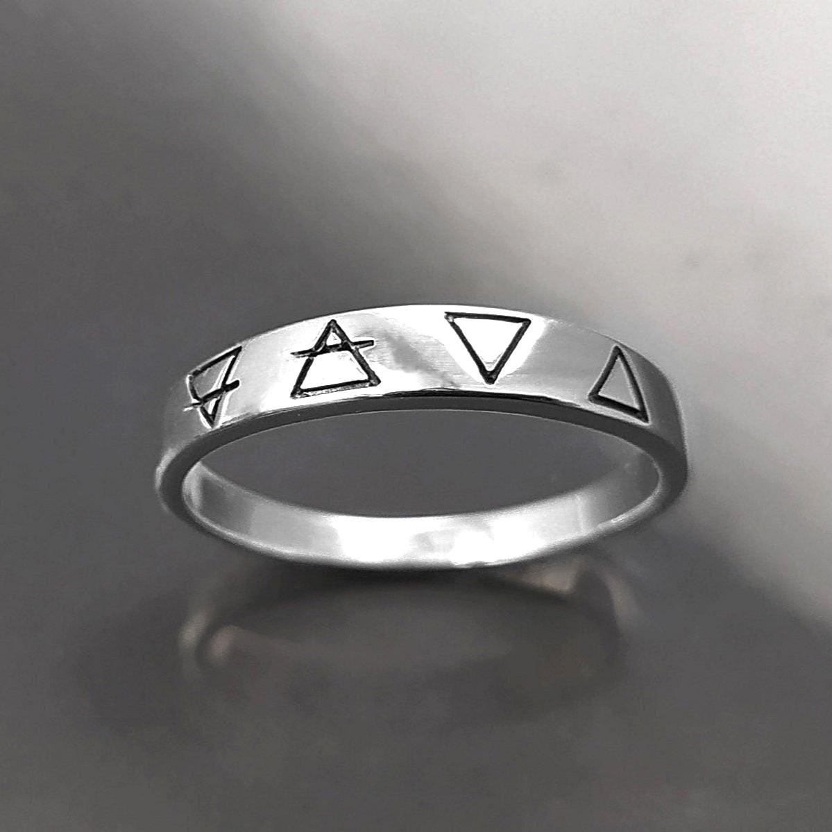 Une bague en argent avec quatre symboles gravés : un cercle avec une ligne qui le traverse, un triangle, un triangle inversé et un triangle avec une ligne qui le traverse.
VU D'en bas.
Bijou artisanal durable. Fait main local. Boutique de confiance recommandée.
