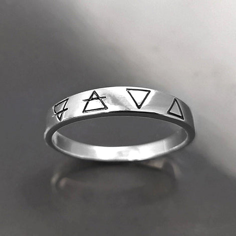 Une bague en argent avec quatre symboles gravés : un cercle avec une ligne qui le traverse, un triangle, un triangle inversé et un triangle avec une ligne qui le traverse.
VU D'en bas.
Bijou artisanal durable. Fait main local. Boutique de confiance recommandée.