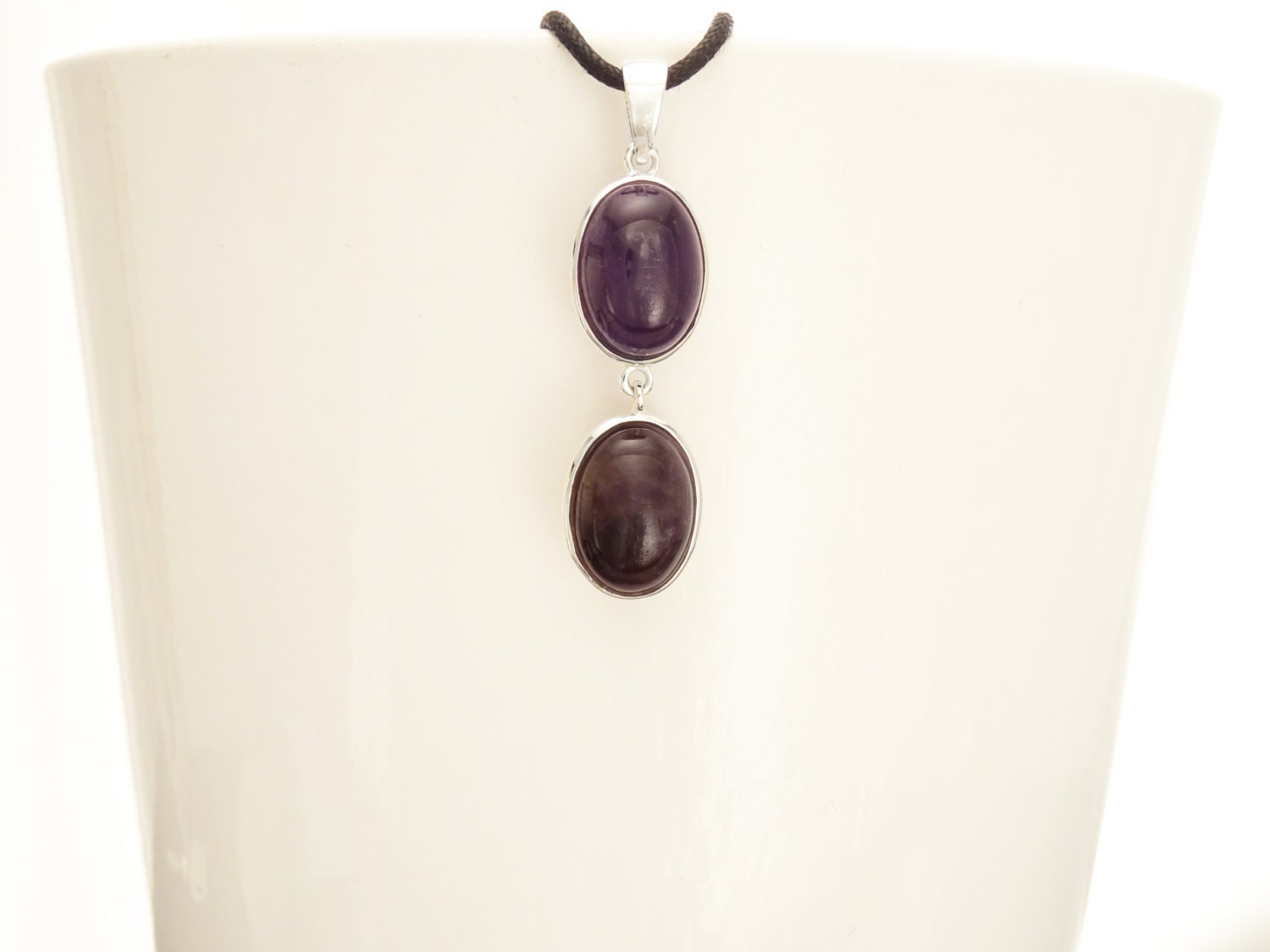 Peut inclure: Un collier en argent avec deux pierres d'améthyste de forme ovale. Les pierres sont d'une couleur violet foncé et sont serties d'argent.
