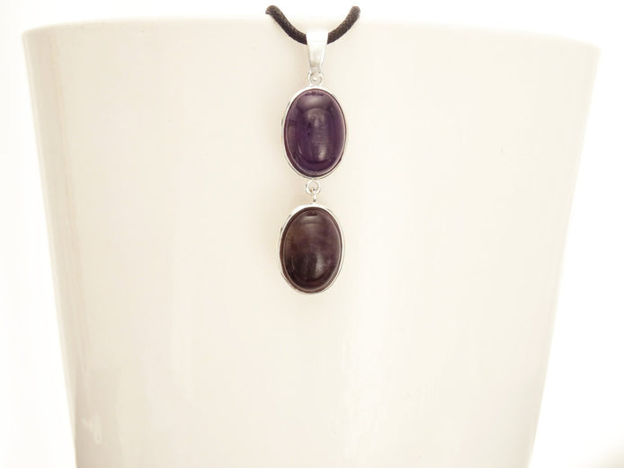 Peut inclure: Un collier en argent avec deux pierres d'améthyste de forme ovale. Les pierres sont d'une couleur violet foncé et sont serties d'argent.