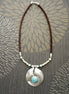 Peut inclure: Un collier en cordon de cuir marron avec un pendentif en argent orné d'une pierre turquoise et d'accents de perles blanches.