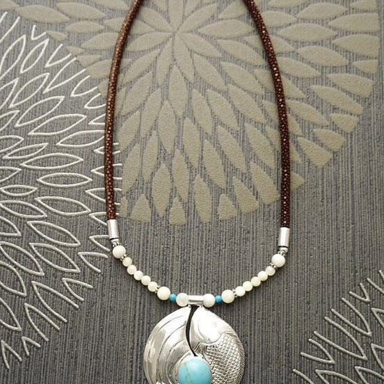 Peut inclure: Un collier en cordon de cuir marron avec un pendentif en argent orné d'une pierre turquoise et d'accents de perles blanches.
