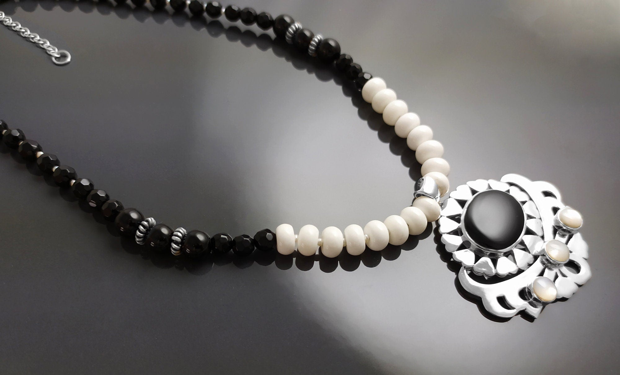 Peut inclure: Un collier de perles noires et blanches avec un pendentif en argent orné d'une pierre d'onyx noire et d'accents en nacre blanche.