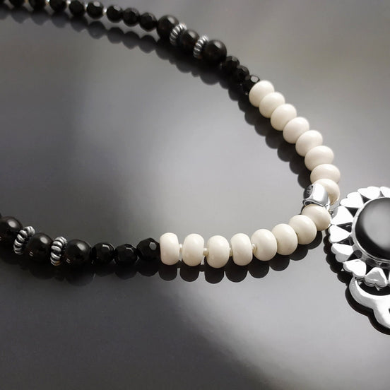 Peut inclure: Un collier de perles noires et blanches avec un pendentif en argent orné d'une pierre d'onyx noire et d'accents en nacre blanche.