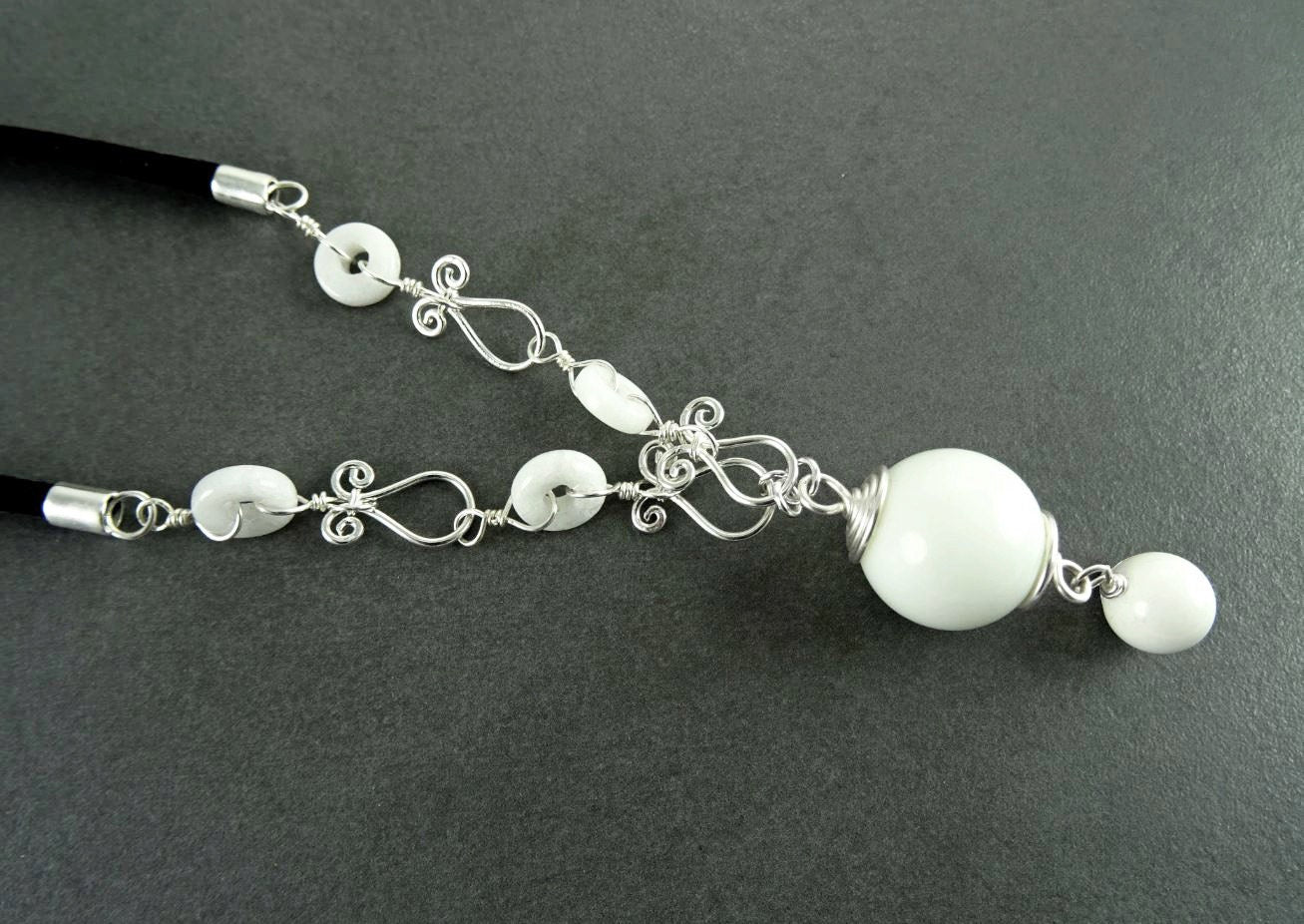 Peut inclure: Un collier blanc avec un grand pendentif blanc et de petites perles blanches. Le collier est fait de fil d'argent et a un design délicat et complexe.