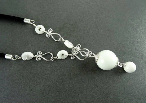 Peut inclure: Un collier blanc avec un grand pendentif blanc et de petites perles blanches. Le collier est fait de fil d'argent et a un design délicat et complexe.