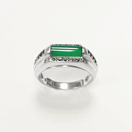 Peut inclure: Une bague en argent avec une pierre verte sertie dans un cadre rectangulaire. Le cadre est décoré de petites pierres noires.
